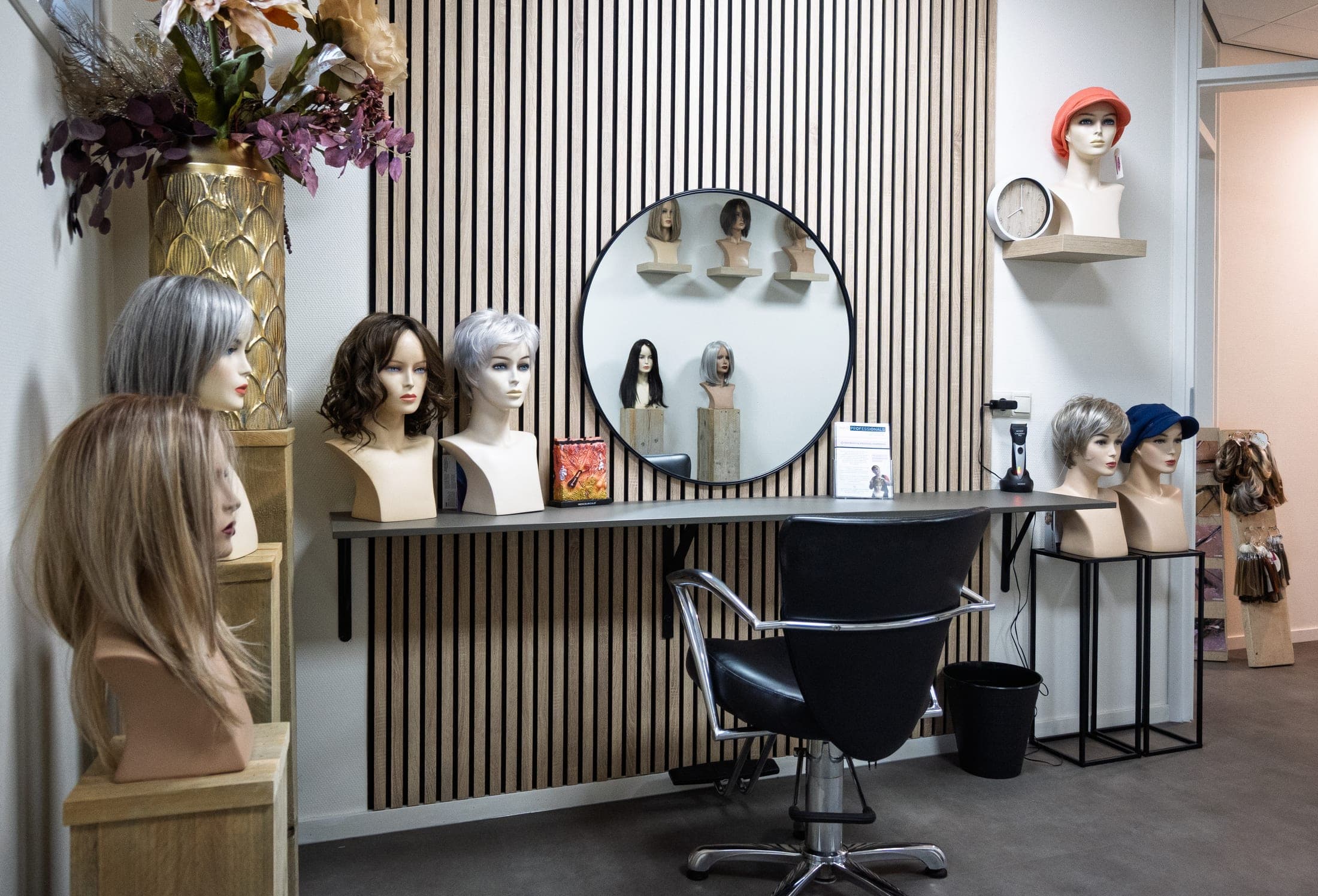 Interieur van Hair Professionals met pruiken op standaards, een ronde spiegel en een stoel.