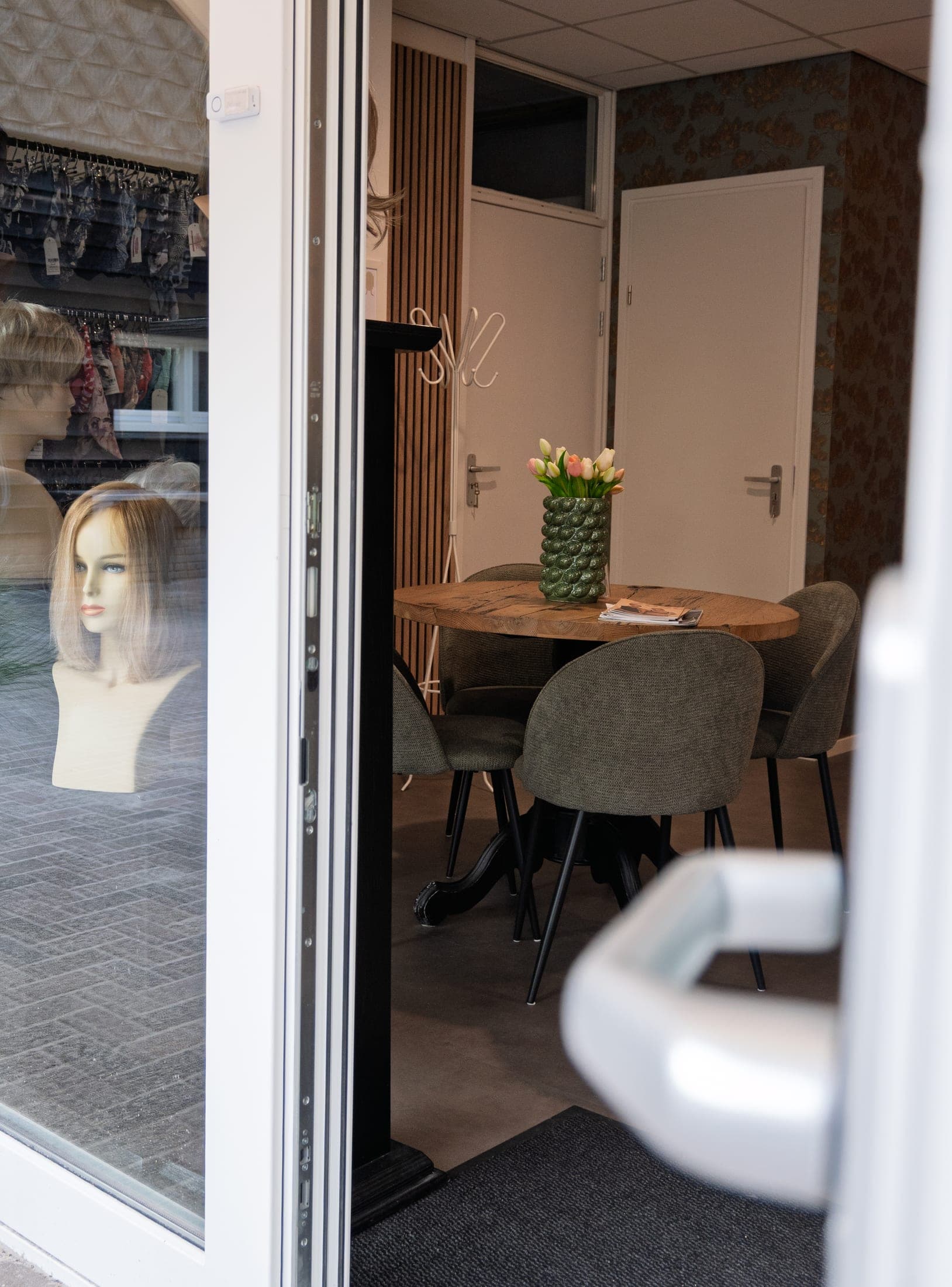 Doorkijk naar de spreekkamer met een ronde tafel, stoelen en verse tulpen.
